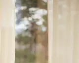 Lätta, ljusa gardiner ramar in en suddig vy av träd. Olika typer av gardiner kan skapa en mjuk atmosfär.