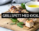 Grillspett med kyckling på en träskärbräda, redo för ett gott grillspett recept. Serveras med en skål med olja och grönsaker.