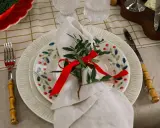 Vacker juldukning dekoration med en tallrik med bär, en vit servett med grönt och rött band, samt bestick med bambuhandtag.