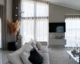 En ljus och luftig vardagsrumsmiljö med en stor soffa, ett soffbord och en TV. Varma gardiner släpper in ett mjukt ljus.