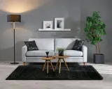 Grå soffa med svarta kuddar, två runda träbord, svart matta och golvlampa. Bra inredningstips för ett modernt vardagsrum.