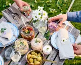 En härlig dukning med vegetarisk midsommarmat: potatissallad, sillinläggningar, gräddfil och hackad rödlök. Blommor och grönska skapar en festlig stämning.