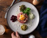 En tallrik med råbiff recept, toppad med äggula, omgiven av hackad rödbet, kapris, persilja, lök och gurka.