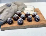 Mörka, chokladöverdragna protein chokladbollar toppade med kokosflingor ligger på en träskärbräda.