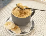 En fluffig mugcake proteinpulver med bananskivor. En sked lyfter en bit av den läckra kakan.