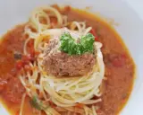 En portion spaghetti med en stor frikadell i en krämig tomatsås, toppad med färsk persilja.