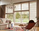 En ljus vardagsrumsmiljö med en bekväm soffa, en färgglad matta och en elegant kristallkrona. En hissgardin på gardinstång ger ett mjukt ljusinsläpp.