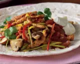 En portion fajitas med kyckling, paprika, champinjoner och lök på en tortilla, serverad med gräddfil. Ett gott fajitas recept!