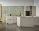 Ett modernt, hållbart kök med beige skåp, grön mosaik och ett runt matbord i trä.