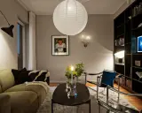 Mysig vardagsrumsmiljö med en stor papperslampa i taket. Belysning bakom gardin skapar en mjuk atmosfär.