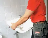 En person i röd tröja och arbetsbyxor håller i ett nytt handfat för att byta ut det gamla.