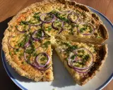 En gyllene ostpaj med rödlök och gräslök, perfekt för ett ostpaj recept. En bit är uppskuren.