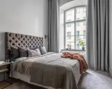 Sovrum med en stor säng, en taklampa och en **gardin på ena sidan av fönstret**.