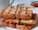 En stapel gyllene franska våfflor, pudrade med florsocker, väntar på att avnjutas. En härlig frukost eller fika.