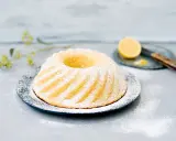 En vacker citronkaka i långpanna, pudrad med florsocker, står på ett fat. En halv citron och en kniv syns i bakgrunden.