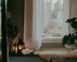 Mysig fönsterbräda med fårskinn, ljuslyktor och tunna gardiner som släpper in ett mjukt ljus.