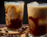 Två glas med krämigt iskaffe, perfekt för ett somrigt iskaffe recept. Kaffebönor sprider sig runt glasen.