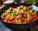 En närbild av en läcker kycklingwok med nudlar, toppad med sesamfrön och färsk koriander. En perfekt måltid!