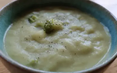 En krämig potatis och broccolisoppa, toppad med lite svartpeppar, serveras i en blå kantad skål.
