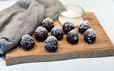 Mörka, chokladöverdragna protein chokladbollar toppade med kokosflingor ligger på en träskärbräda.