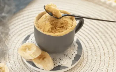 En fluffig mugcake proteinpulver med bananskivor. En sked lyfter en bit av den läckra kakan.
