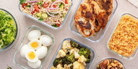 Förberedd student mat i glasbehållare: kycklingfilé, couscoussallad, grönsaker, ägg och nötter. Perfekt för en hälsosam lunchlåda.