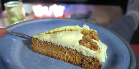 En bit saftig glutenfri morotskaka med krämig frosting och valnötter på en blå tallrik.