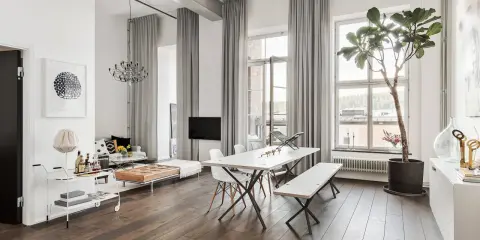 En modern lägenhet med en lång gardinstång vägg till vägg som ramar in stora fönster. Ljusa gardiner skapar en mjuk atmosfär.