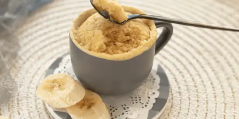 En fluffig mugcake proteinpulver med bananskivor. En sked lyfter en bit av den läckra kakan.