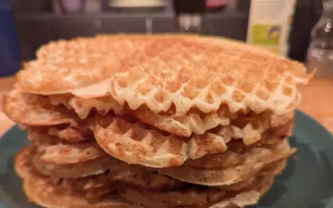 En hög med gyllene, glutenfria våfflor på en grön tallrik. Perfekt för en frukost eller fika!