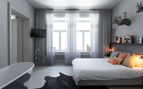 Sovrum med badkar, säng och en **gardin en sida** som ramar in fönstren.