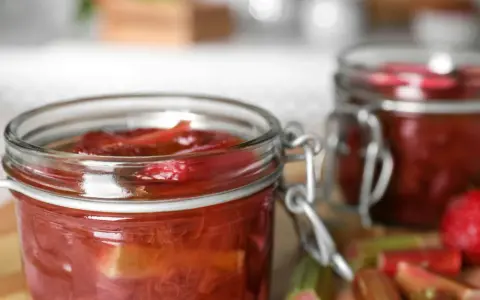 Två glasburkar med rabarberkompott, perfekt för ett gott rabarber recept. Färska rabarberstjälkar syns i förgrunden.
