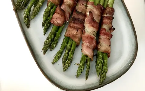 Grön sparris insvept i knaprigt bacon, serverad på en ljusblå tallrik. En läcker och enkel rätt som passar till det mesta.