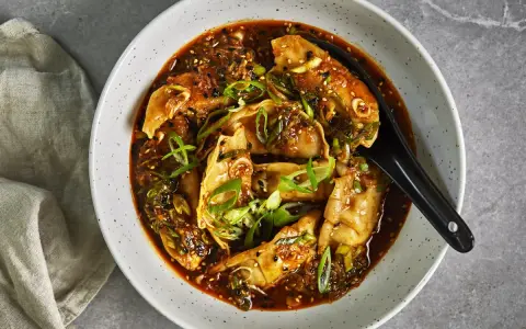 En skål med dumplings i en kryddig sås, toppad med salladslök och sesamfrön. Ett perfekt recept middag för en smakrik kväll.