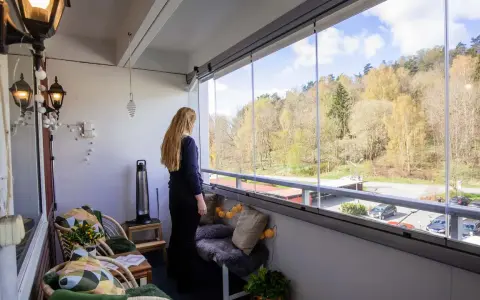 Kvinna njuter av utsikten från inglasad balkong. Mysiga sittplatser och lampor ger fina balkong tips för en ombonad känsla.