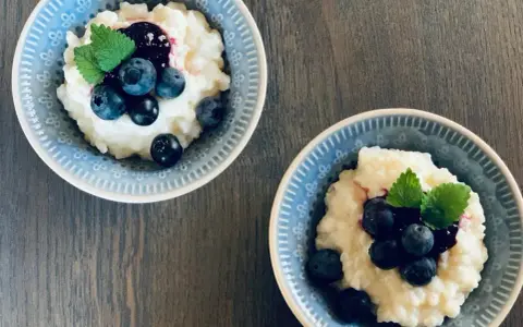 Två skålar med krämig risgrynsgröt, toppad med blåbär och mynta. Ett enkelt och gott risifrutti recept.