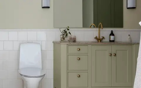 Ett modernt badrum med toalett och ett grönt badrumsskåp med mässingsdetaljer.