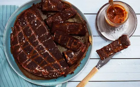 Chokladkaka med kolasås och havssalt, perfekt att baka glutenfritt. En bit lyfts upp med en kniv.