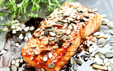 En saftig bit teriyaki lax toppad med frön, serverad i en glansig sås med gröna örter.