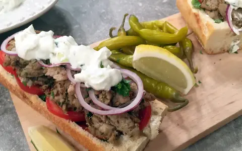 En saftig gyros i baguette med tomater, rödlök och tzatziki. Serveras med pepparfrukter och citronklyfta. Ett perfekt gyros recept!