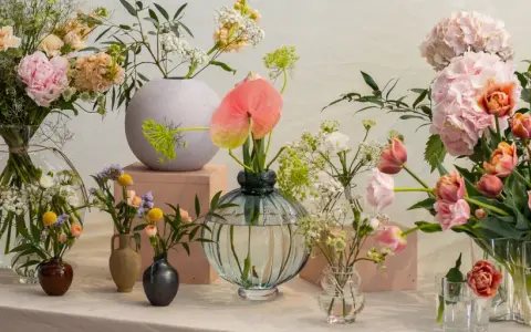 En samling vaser med olika typer av blommor, inklusive pioner, tulpaner och hortensior i mjuka pastellfärger.