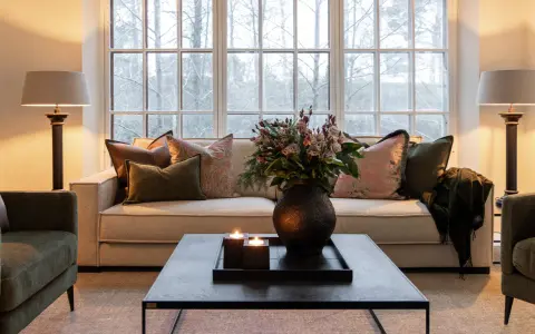 En soffgrupp med klassisk design, prydd med kuddar och en bukett blommor. Två golvlampor ger ett varmt sken.