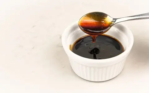 En sked häller mörk, glansig teriyakisås i en vit skål. Perfekt för ditt teriyakisås recept.