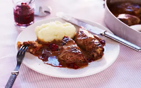 Kåldolmar recept: två kåldolmar med potatismos och lingonsylt, serverade på en tallrik med en gaffel och kniv.