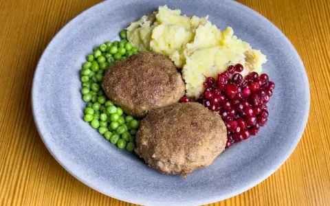 Två köttbullar med potatismos, gröna ärtor och rårörda lingon. En klassisk tallrik med svensk husmanskost.