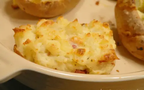 En närbild på en krämig, gratinerad bakad potatis fylld med ost och bacon. En riktig favorit!