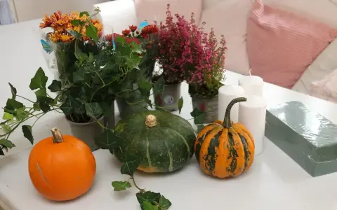 Förberedelser för att dekorera pumpa med höstblommor, ljus och murgröna.
