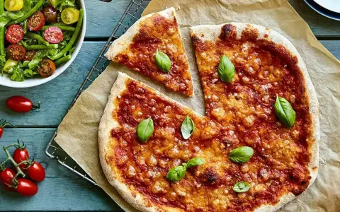 En härlig hemmagjord pizza med tomatsås och ost, toppad med färsk basilika. Bredvid en fräsch sallad med gröna bönor och tomater.