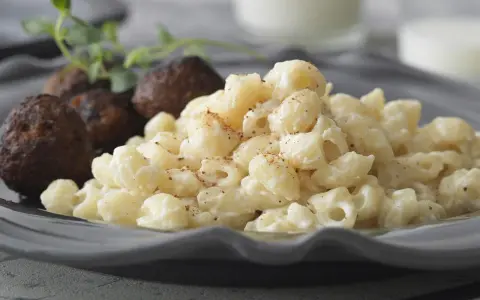 En tallrik med stuvade makaroner och köttbullar, garnerad med en kvist örter. En klassisk svensk rätt som väcker aptit.