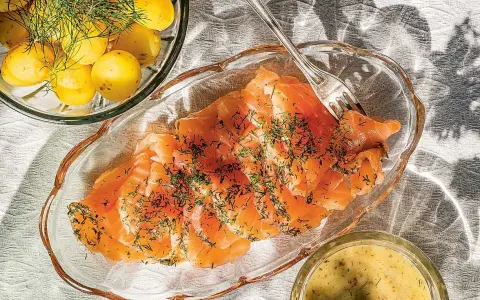 Gravlaxsås recept: Skivad gravad lax med dill, serverad med kokt färskpotatis och en skål med gravlaxsås.